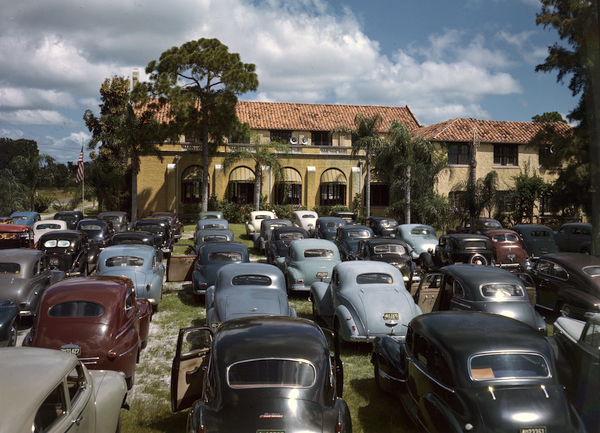 Cars from the 1940s are parked in front of a church during a drive-in church service